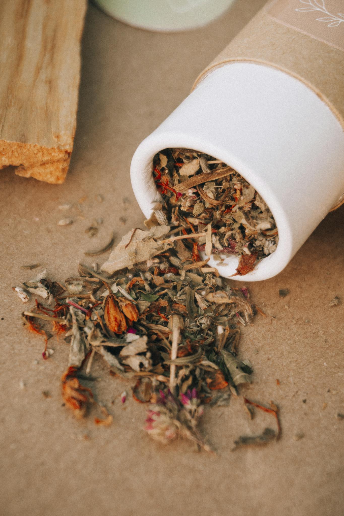 A close-up of dried herbs spilling from a cardboard tube in a natural setting.
