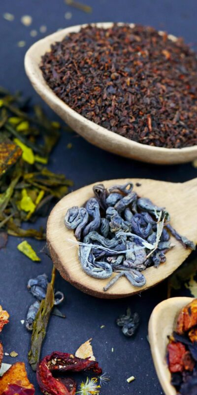 Assorted loose leaf herbal teas in wooden spoons on a flat lay composition, showcasing various colors and textures.